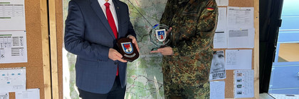 Zwei Personen stehen vor einer Pinnwand und halten getauschte Wappen in der Hand - Klick öffnet Bildbetrachter
