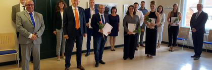 Die Absolventen sowie ihre Begleiter stehen mit Landrat Roger Lewandowski in einem Raum und schauen in die Kamera.