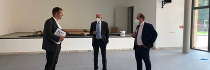 Drei Männer stehen im Halbkreis und unterhalten sich in der noch leeren neuen Halle.