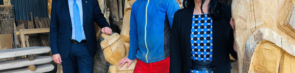 Drei Personen stehen zwischen großen Holzskulpturen - Klick öffnet Bildbetrachter