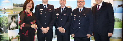 Drei Feuerwehrleute stehen zwischen der Kreistagsvorsitzenden und dem Landrat und lächeln in die Kamera.