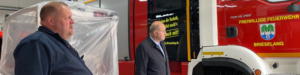 Zwei Männer stehen neben einem Feuerwehrauto.