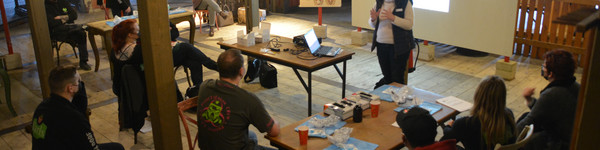 Eine Gruppe von Menschen sitzt in einem Raum. Eine Person steht vor der Gruppe und erklärt etwas.