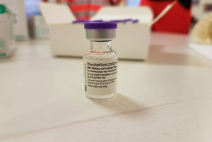 Eine Ampulle des Impfstoffes steht auf einem Tisch.