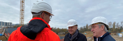 Drei Männer stehen auf einer Baustelle und unterhalten sich.