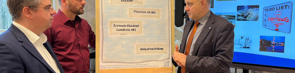 Drei Männer stehen vor einem Flipchart und unterhalten sich - Klick öffnet Bildbetrachter