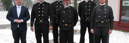 Sechs Männer, darunter fünf Schornsteinfeger stehen in einer Gruppe und schauen in die Kamera.