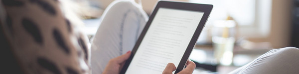 Eine Frau sitzt auf einem Lesestuhl und liest in einem E-Book.