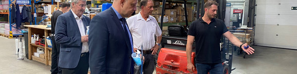 Vier Männer stehen in einer Lagerhalle, einer von ihnen zeigt auf etwas und redet.