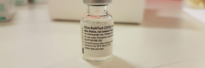 Eine Ampulle des Impfstoffes steht auf einem Tisch.