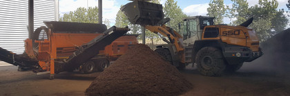 Ein Bagger schüttet Abfall in die Kompostieranlage, davor liegt ein großer Haufen Kompost - Klick öffnet Bildbetrachter