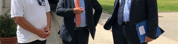 Drei Männer stehen auf dem Vereinsgelände und unterhalten sich.