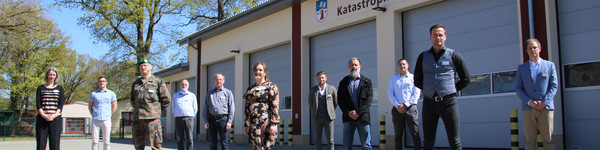 Die Mitglieder des havelländischen Corona-Krisenstabes stehen vor einer Fahrzeughalle.