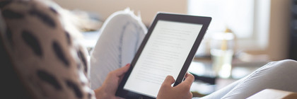 Eine Frau sitzt auf einem Lesestuhl und liest in einem E-Book.