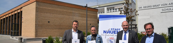 Vier Personen stehen vor einer Schule und halten jeweils eine Mappe in der Hand - Klick öffnet Bildbetrachter