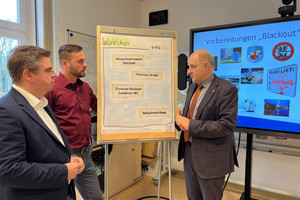 Drei Männer stehen vor einem Flipchart und unterhalten sich - Klick öffnet Bildbetrachter