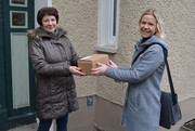 Zwei Frauen stehen vor einem Haus. Zwischen ihnen ist ein Paket.