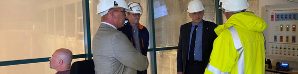 Vier Männer stehen im Kreis, im Hintergrund ist die Müllverbrennungsanlage zu sehen.