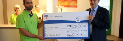 Dr. Wilke und Landrat Lewandowski stehen in der Arztpraxis und halten einen symbolischen Scheck zwischen sich.