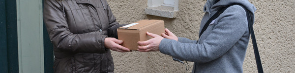 Zwei Frauen stehen vor einem Haus. Zwischen ihnen ist ein Paket.