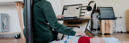 Eine Frau arbeitet am Computer und streichelt nebenbei ihr kleines Kind.