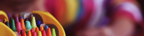 Eine Box mit bunten Stiften, im Hintergrund malt ein Kind.