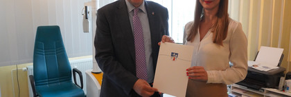 Der Landrat und die Ärztin stehen in einem Behandlungszimmer und halten zwischen sich eine Mappe mit Landkreiswappen - Klick öffnet Bildbetrachter