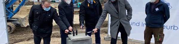 Vier Männer mit einem Hammer in der Hand stehen verteilt um den Grundstein herum.