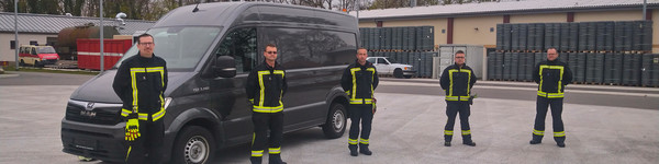 Fünf Männer in Feuerwehrkleidung stehen vor einem Trasporter.