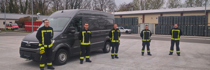 Fünf Männer in Feuerwehrkleidung stehen vor einem Trasporter.