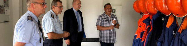 Vier Männer stehen in einem Umkleideraum der Feuerwehr.