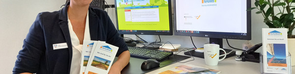 Eine Frau steht am Schreibtisch und hält Flyer in den Händen.