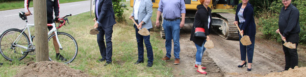 Mehrere Menschen stehen in einer Reihe und führen einen Spatenstich aus.