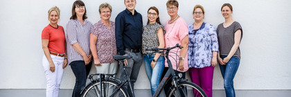 Acht Personen stehen vor einer Wand, davor steht ein Fahrrad - Klick öffnet Bildbetrachter