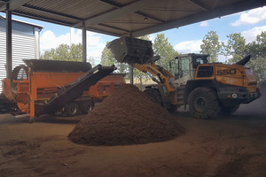 Ein Bagger schüttet Abfall in die Kompostieranlage, davor liegt ein großer Haufen Kompost - Klick öffnet Bildbetrachter