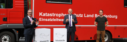 Harry Bräuer, Roger Lewandowski und Christoph Bajohr stehen vor einem Rettungsfahrzeug und zeigen zwei Schutzbrillen.