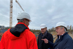 Drei Männer stehen auf einer Baustelle und unterhalten sich.