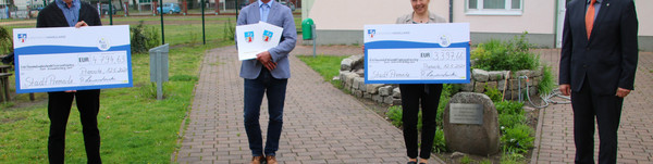 Die beiden Schulleiter, der Bürgermeister und der Landrat stehen auf dem Außengelände der Oberschule in Premnitz. Die Schulleiter halten einen großen Scheck in den Händen, auf dem die jeweilige Fördersumme vermerkt ist.