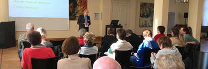 Klick öffnet Bildbetrachter, Mann spricht vor Gruppe von Menschen