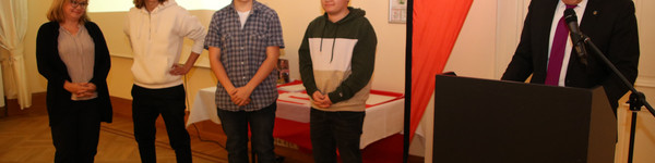 Der Landrat steht am Rednerpult und hält eine Laudatio. Daneben stehen die Preisträger.