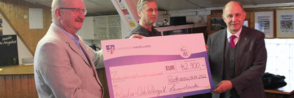 Drei Männer stehen in einem Raum und halten gemeinsam einen großen Scheck in den Händen.