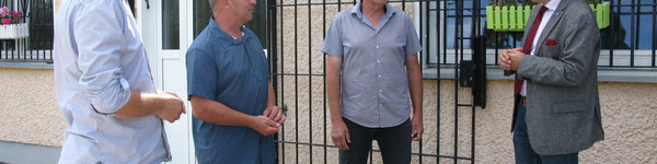 Landrat Lewandowski unterhält sich mit drei Mitgliedern des ESV Lok Elstal vor einem Vereinsgebäude.