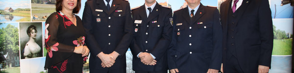 Drei Feuerwehrleute stehen zwischen der Kreistagsvorsitzenden und dem Landrat und lächeln in die Kamera.