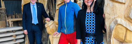 Drei Personen stehen zwischen großen Holzskulpturen - Klick öffnet Bildbetrachter