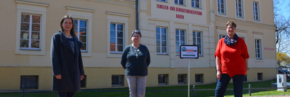 Drei Frauen stehen auf einem Platz, im Hintergrund ist das FGZ Nauen zu sehen.