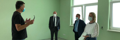 Vier Personen stehen in einem grün gestrichenen Raum und reden miteinander.