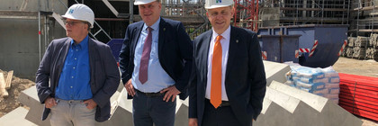 Drei Männer mit Bauhelm stehen auf einer Baustelle.