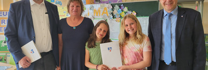 Fünf Personen stehen in einem Klassenraum, im Hintergrund die Tafel und Projektplakate an der Wand - Klick öffnet Bildbetrachter