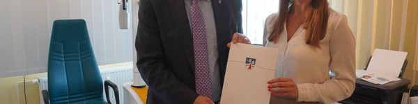 Der Landrat und die Ärztin stehen in einem Behandlungszimmer und halten zwischen sich eine Mappe mit Landkreiswappen - Klick öffnet Bildbetrachter