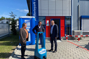 Drei Männer stehen vor einer Dixi-Toilette und unterhalten sich.